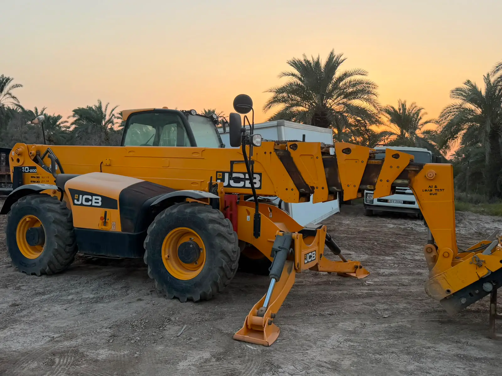 Telehandler with its stabilizers down at sunset, date palms behind